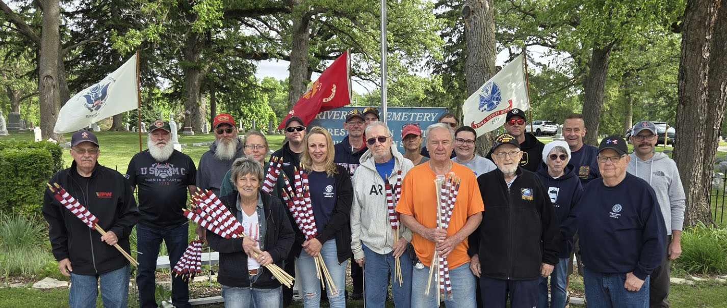 Volunteers gathered at the Riverview Cemetery entrance with American, Marine Corps, and service flags on Memorial Day 2026