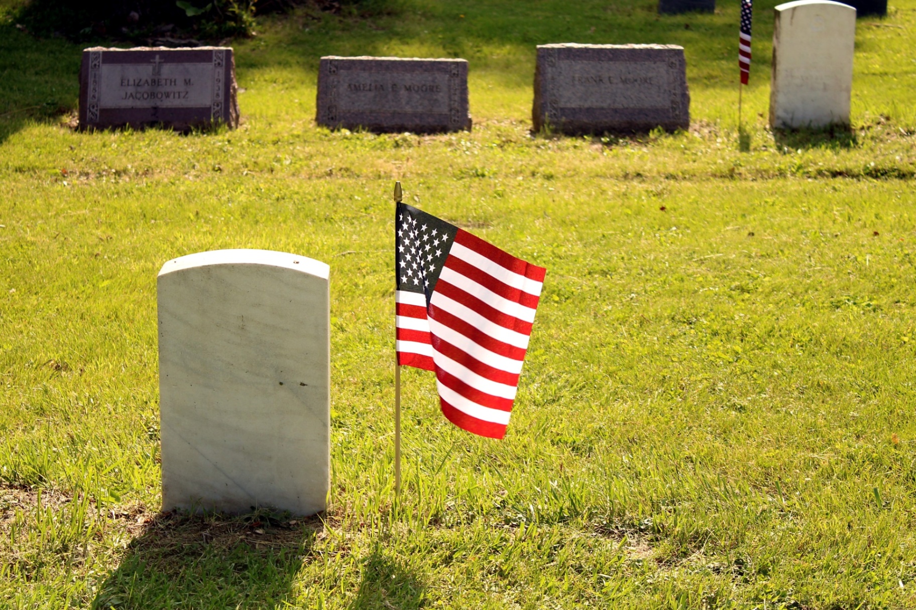 American flag standing beside a weathered marble headstone